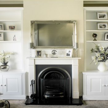 White painted fitted alcove cupboards either side of a period cast iron fireplace with open shelving and display objects above