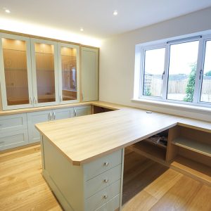 Fitted home office with large L-shaped oak desk, glazed overhead cabinets and base drawer storage
