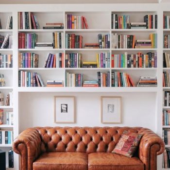 Bespoke built-in bookcases wall to wall in white — floor to ceiling open shelving with central breakfront section and Chesterfield sofa in a living room