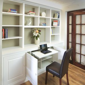 Built in HomeWhite painted fitted home office with pull-out desk concealed within base cupboards, floor-to-ceiling open shelving above office in Cupboards with pullout desk