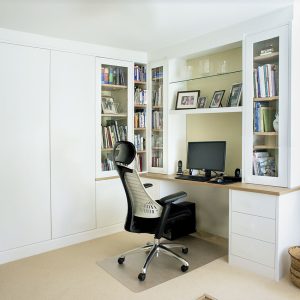 Modern white painted fitted home office with floor-to-ceiling open shelving, integrated desk and base cupboards