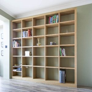 Natural oak fitted bookcases with open cube shelving, filled with books and small ornaments, in a living room.