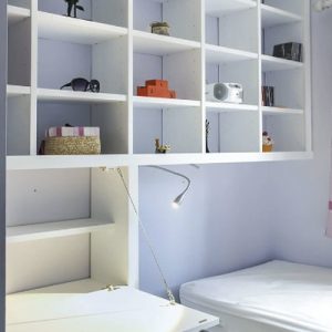 White fitted box shelving with a fold down desk and an integrated reading light, built into a small alcove.